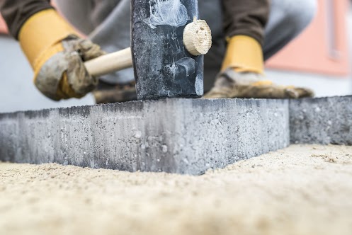 critical areas Builder tamping down a new paving slab or brick with a large mallet in a close up view on the hands and tool.